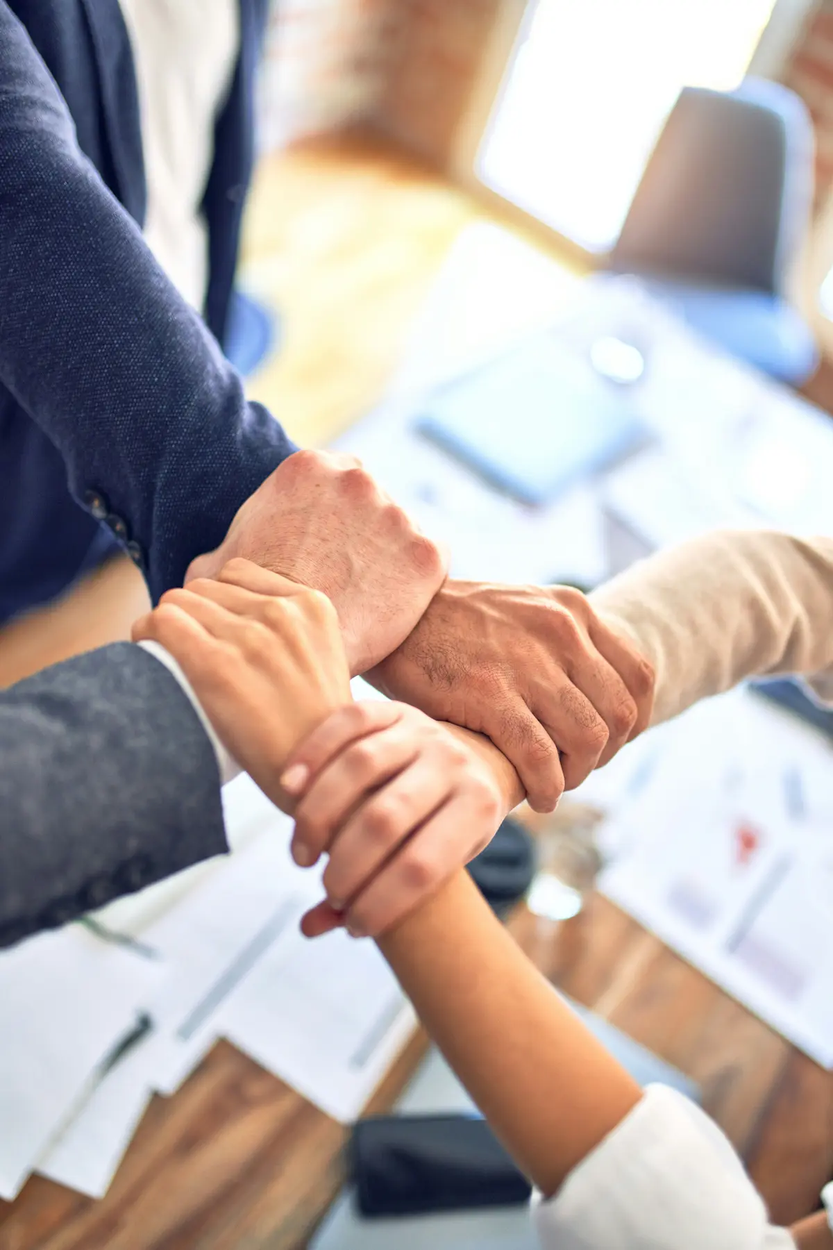 Quatre collègues joignent les mains en cercle au-dessus d'un bureau, symbole de partenariat